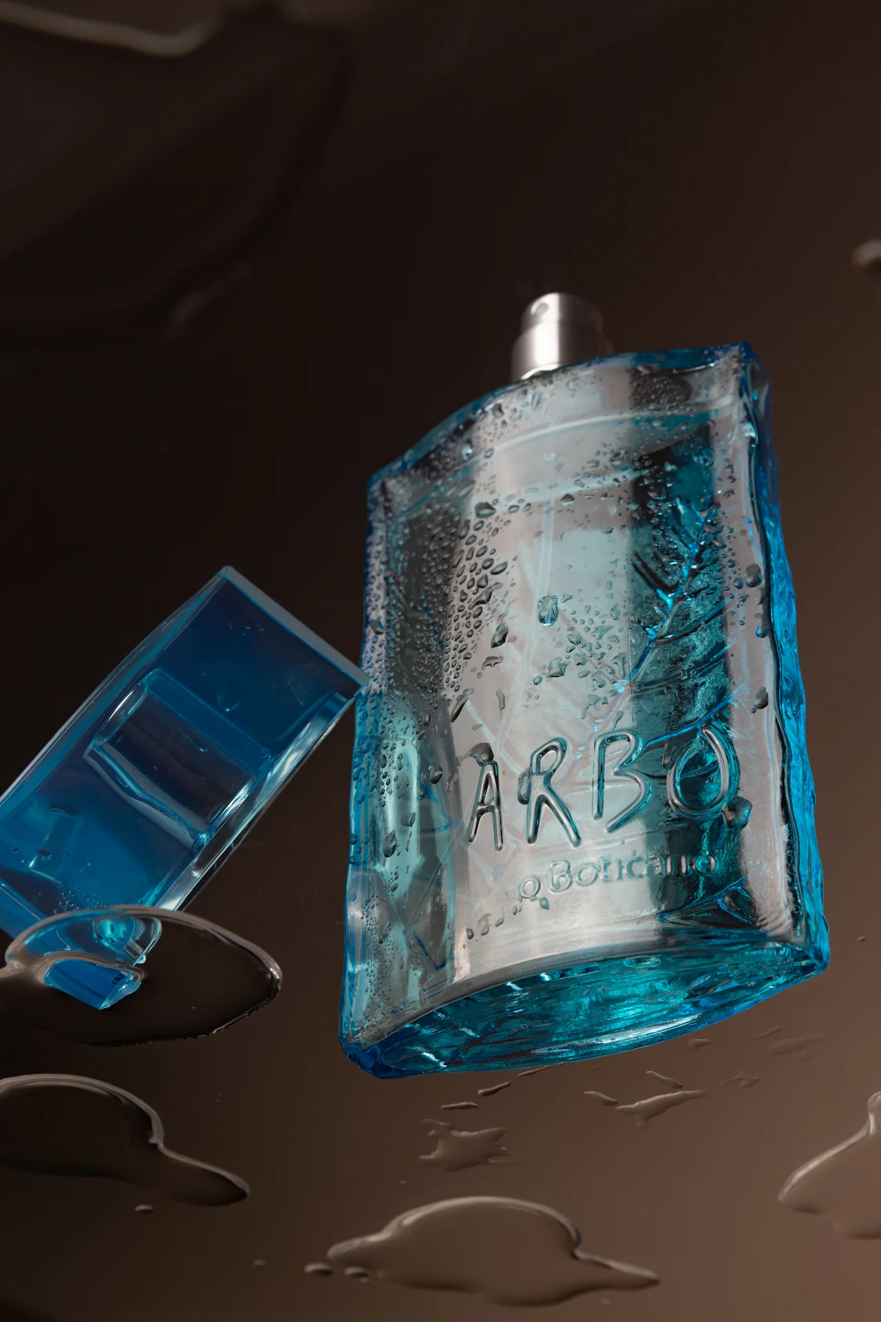 Perfume Boticário em cima de uma superfície de vidro com líquidos, vistos de baixo para realçar o produto